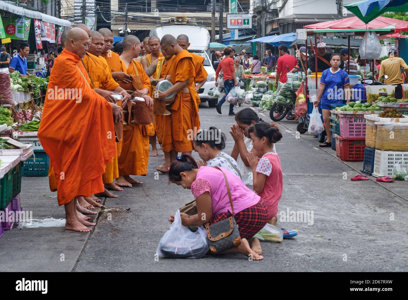 In a market in Phuket Town, Thailand, women kneel and pray in front of Buddhist monks out on their traditional morning alms' round (binta baat) Stock Photo
