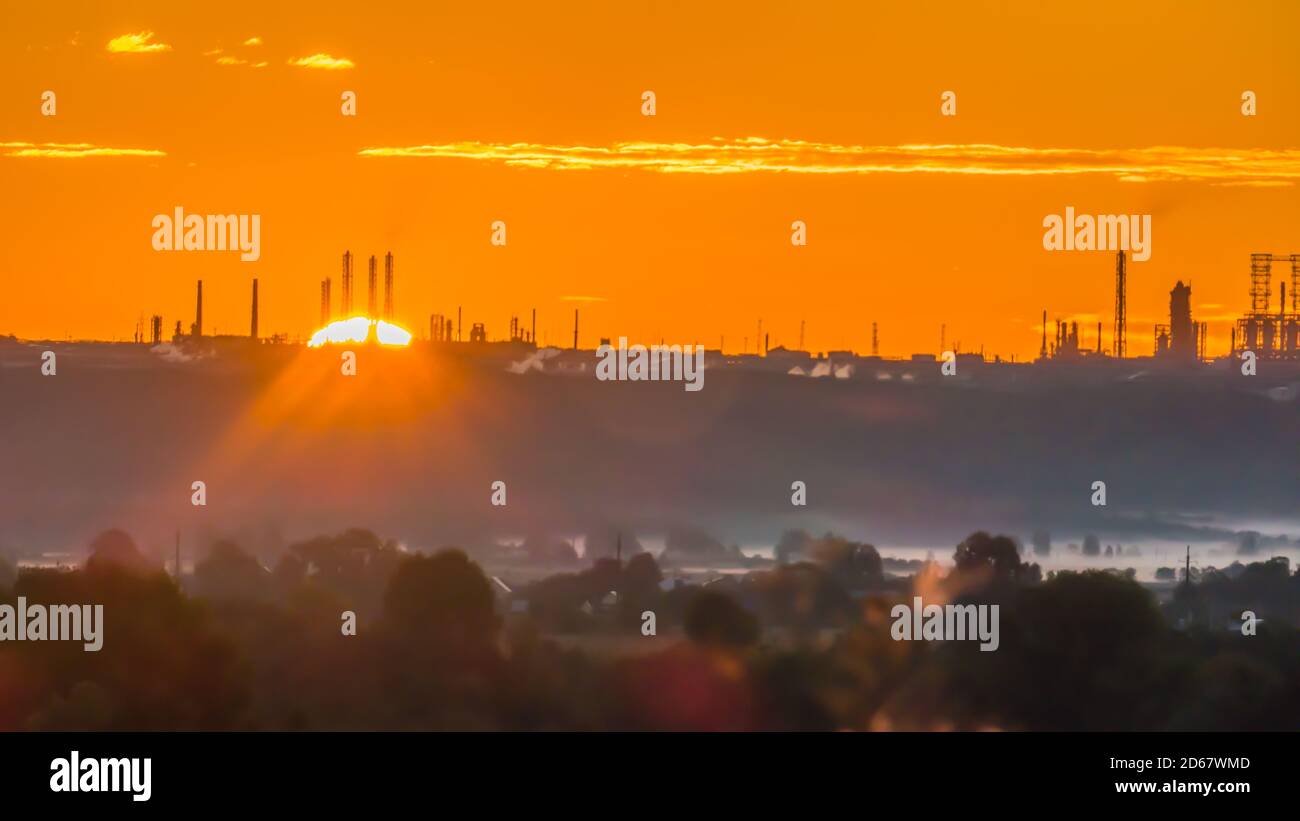 Scarlet sunrise over a chemical plant with pipes at the edge of a forest with a misty hollow Stock Photo