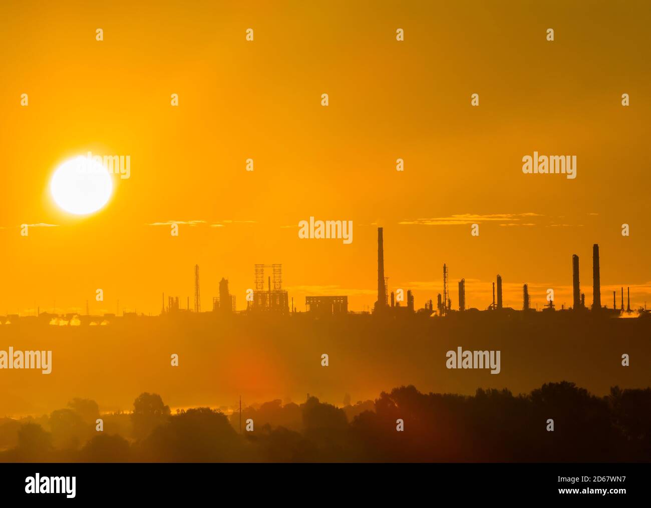 Rising sun over an oil refinery. Scarlet dawn over a petrochemical industry at the edge of a floodplain forest in early autumn morning Stock Photo