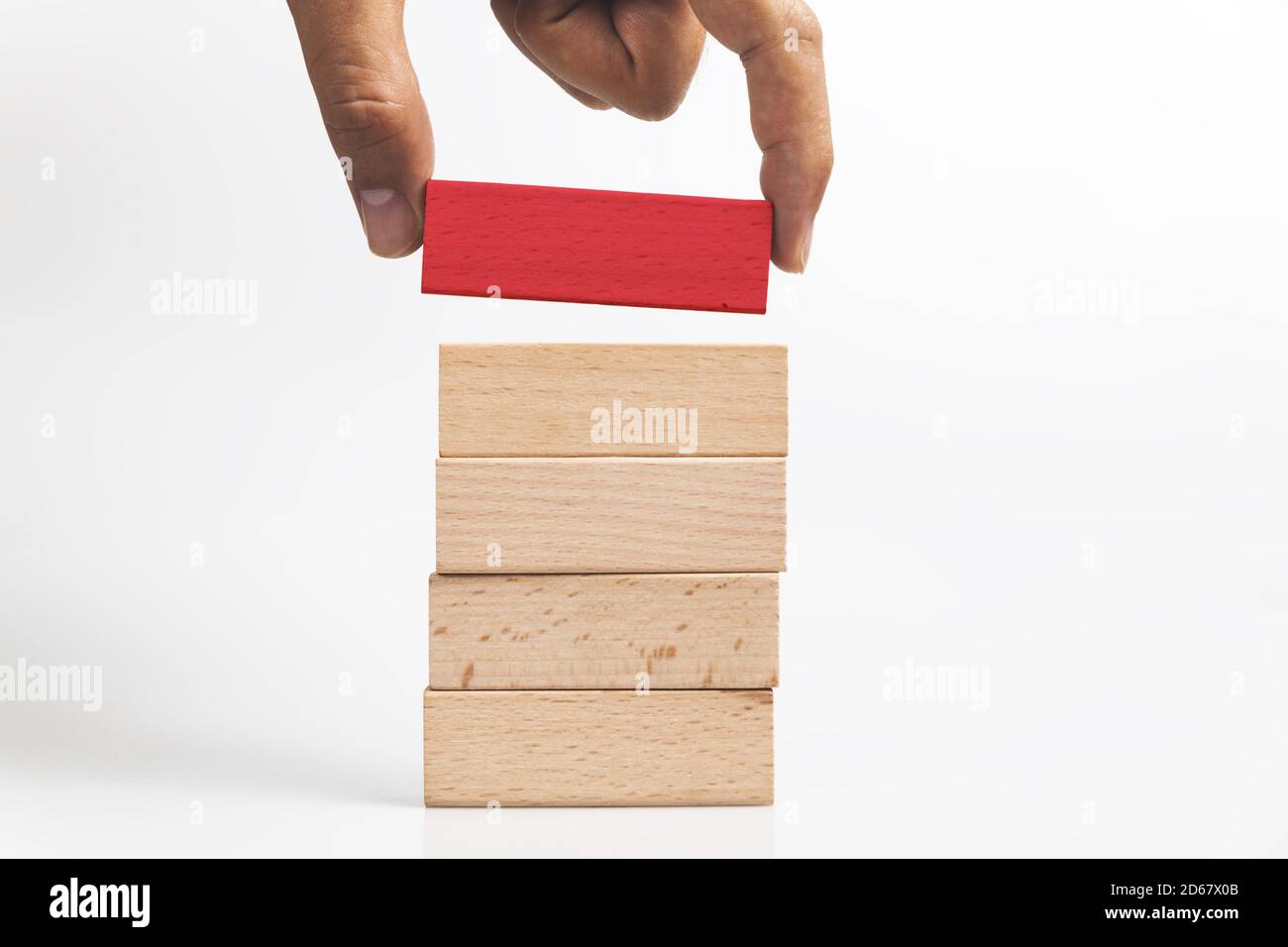 Human hand adding the wooden red block out of the wooden block tower ...