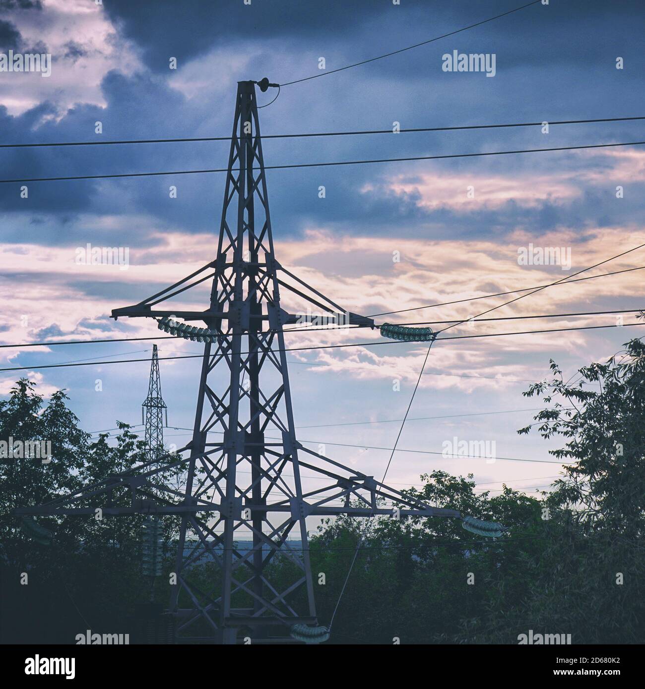 Silhouette of a high-voltage power line tower against cloudy sky in the ...