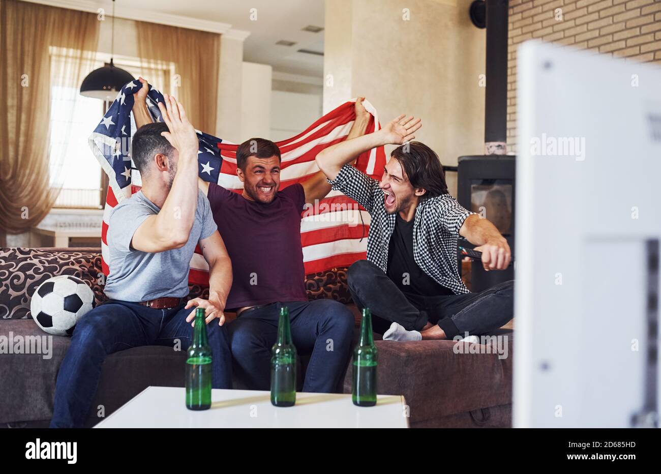 Excited three friends watching soccer on TV at home together Stock Photo