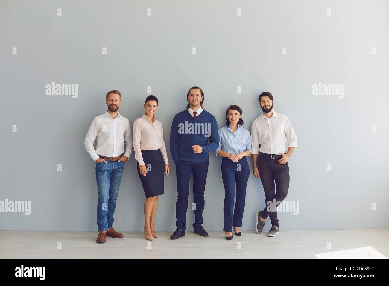 Group portrait of happy businesspeople standing near office wall looking at camera Stock Photo