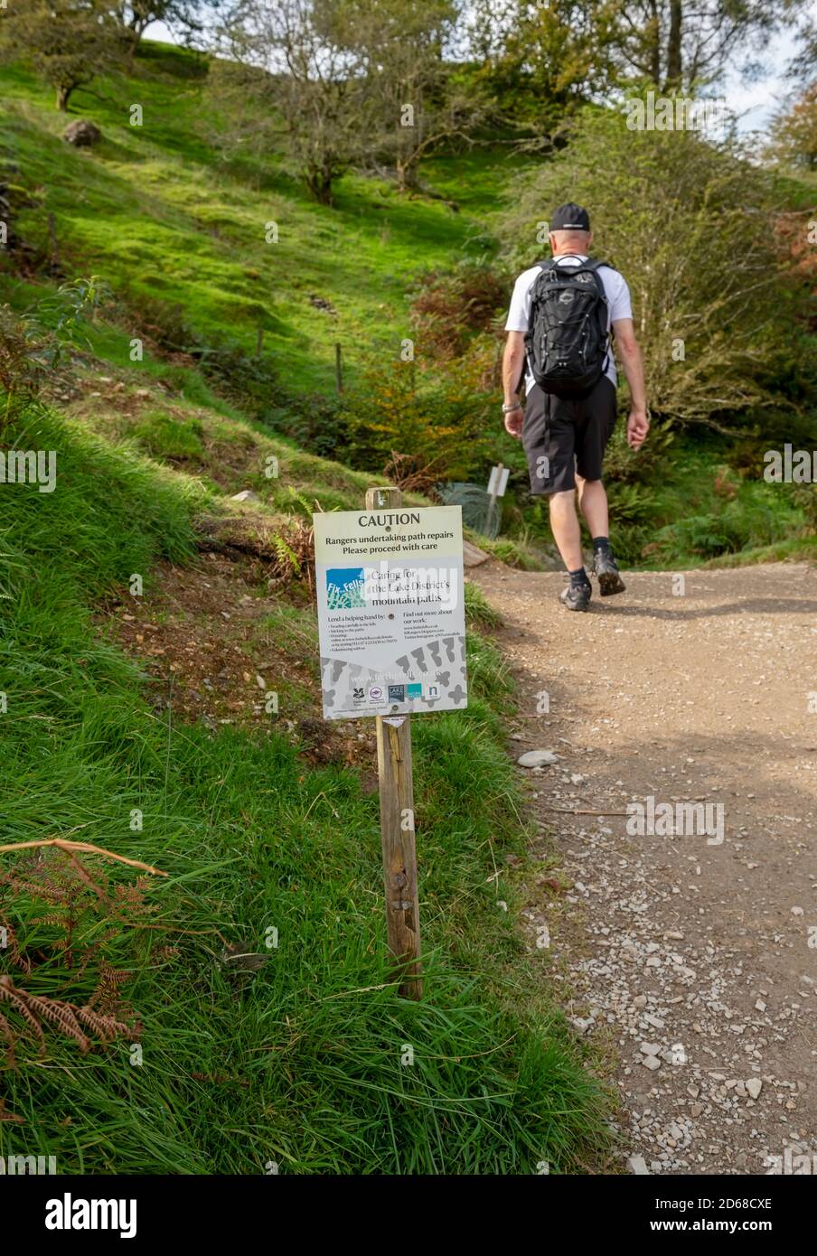 Walker man person walking along footpath at Loughrigg Fell with ‘Fix the fells’ sign beside the path Cumbria Lake District England UK GB Great Britain Stock Photo
