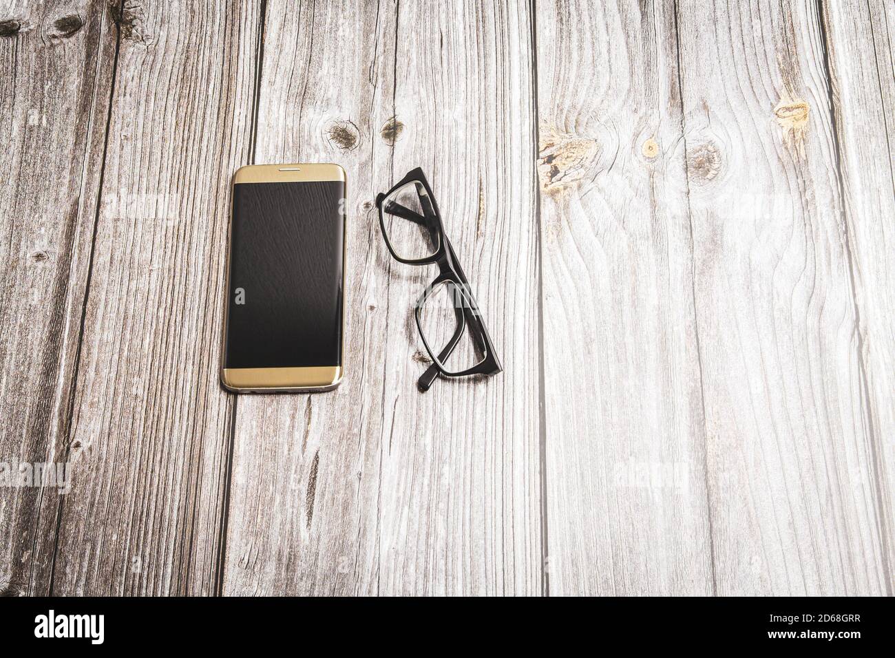 A generic mobile phone or cell phone and a pair of glasses laid on a rustic wooden desk Stock Photo