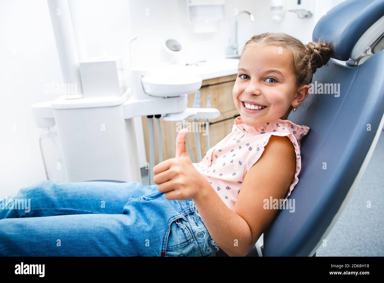 Happy little girl with a perfect white smile showing thumbs up, she sitting in a dental chair. She have healthy teeth Stock Photo
