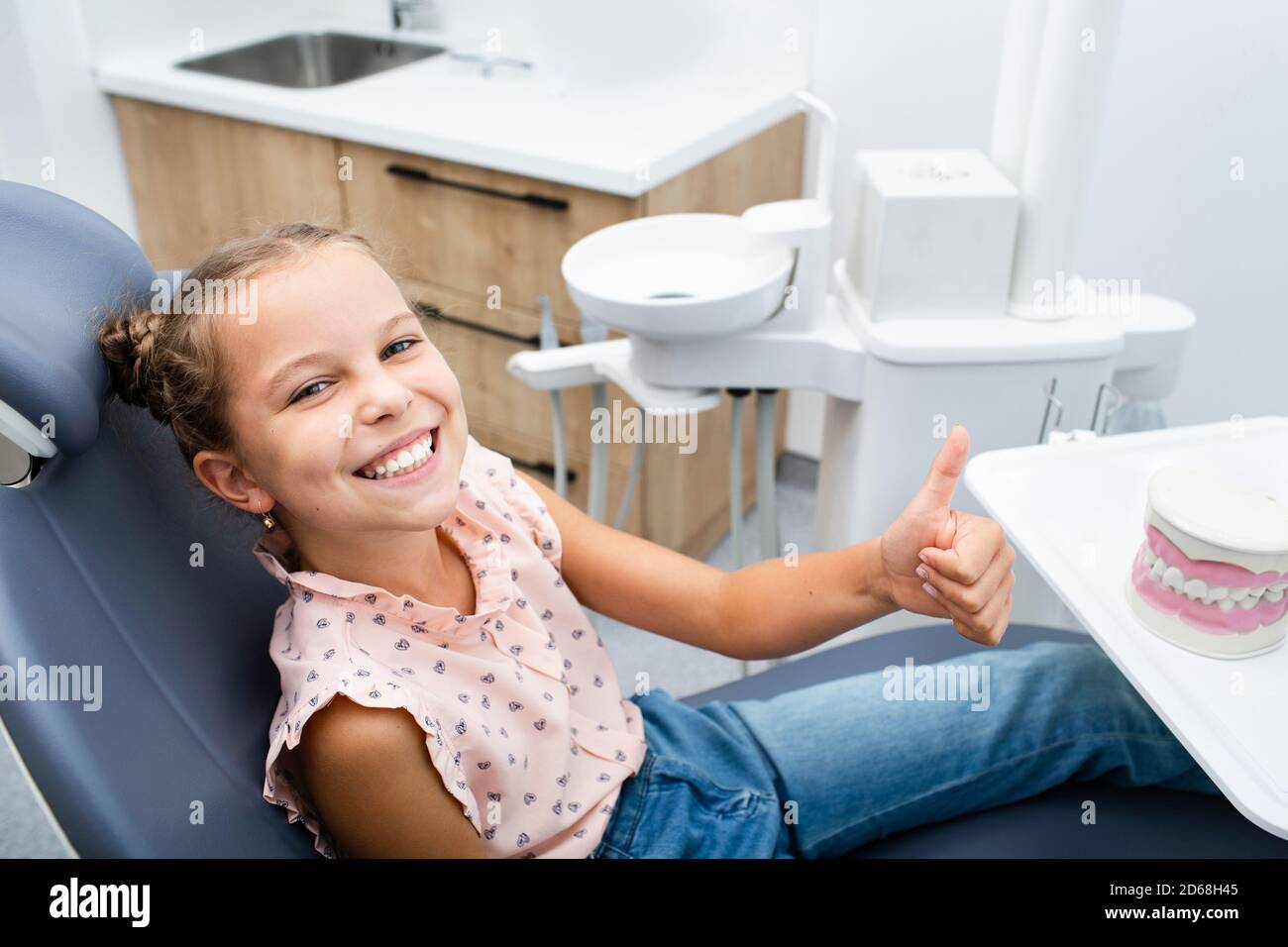 Very happy smiling girl sitting on a dental chair and showing thumbs up. Stock Photo