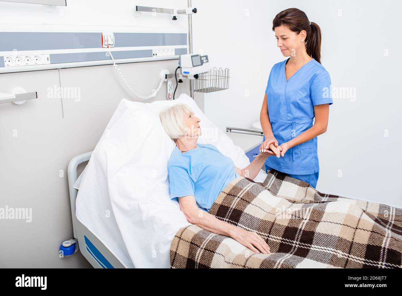 Nurse provides support to a lying senior patient in a hospital room. Rehabilitation after stroke and heart attack in the elderly people Stock Photo