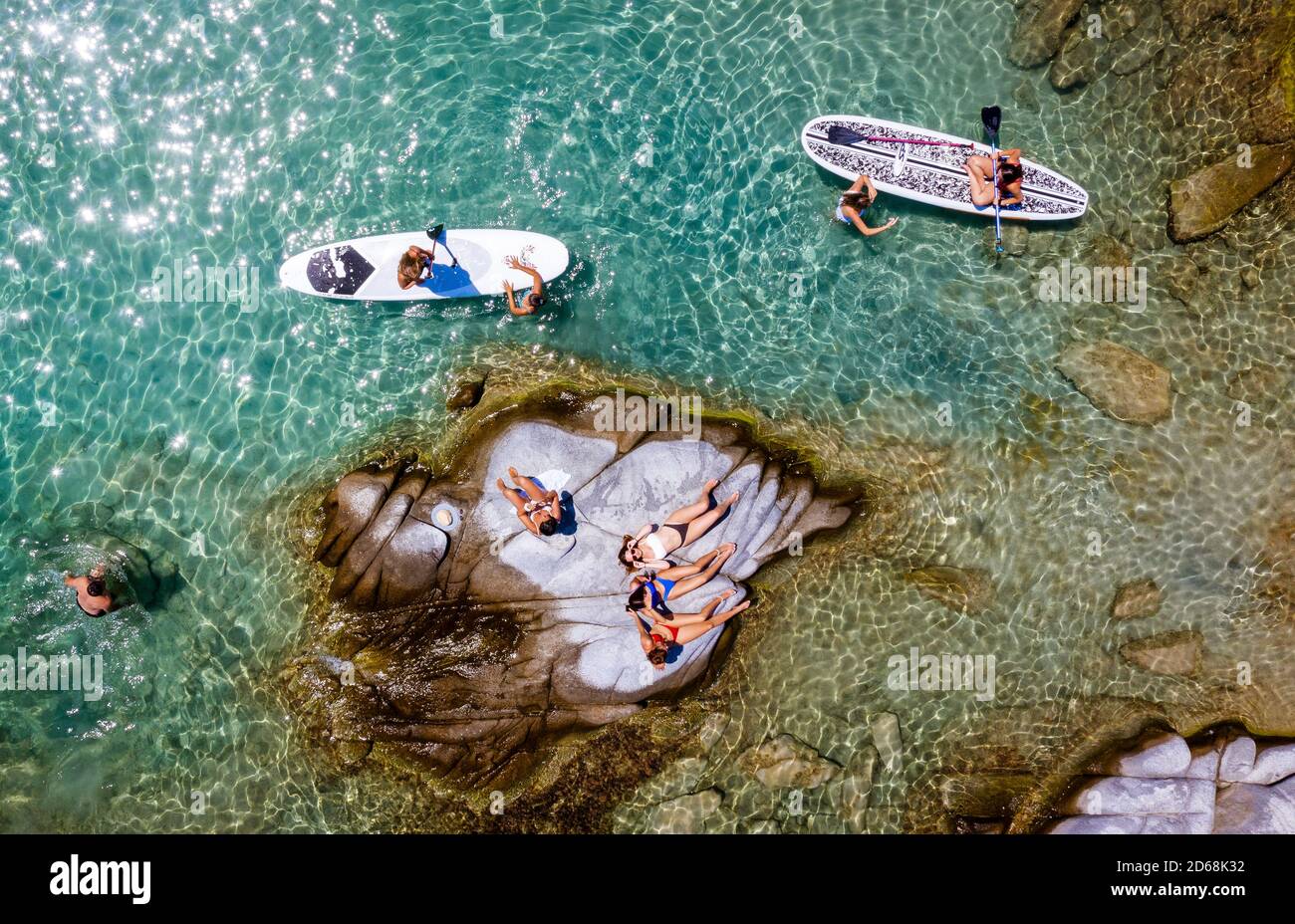 An aerial shot of a beach in Greece with teenagers sunbathing and paddleboarding. Stock Photo