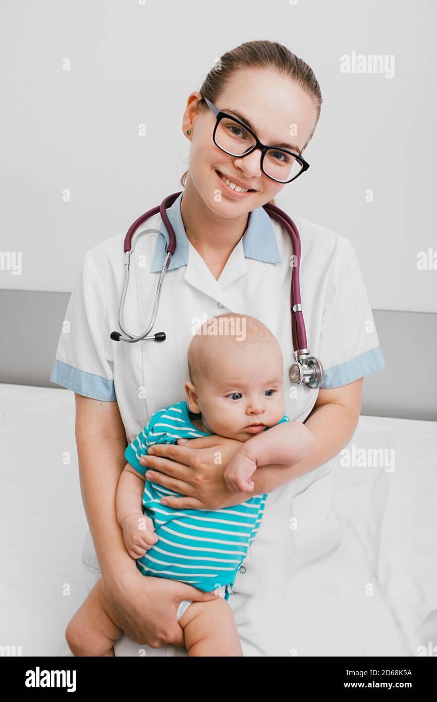 Positive pediatrician holding a baby, she sitting with child on a hospital bed. Care about infant health Stock Photo