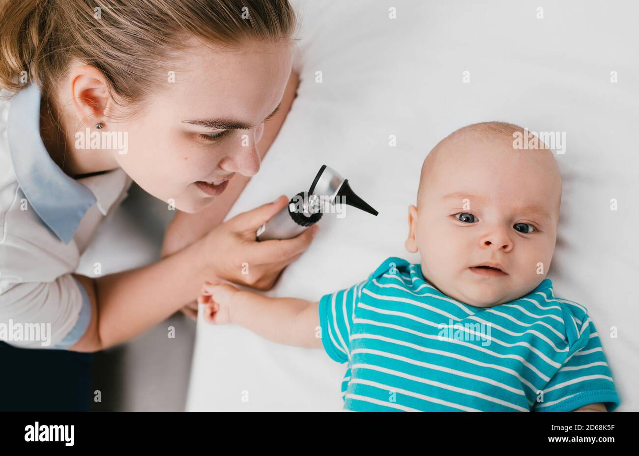Smiling pediatrician doing ear exam with an otoscope to a baby at the hospital. doctor examines infant baby 3-month-old Stock Photo
