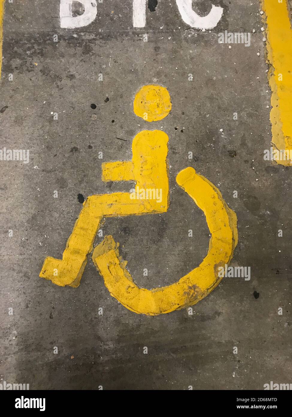 a Sign of a yellow person and wheelchair on the floor in a parkinglot