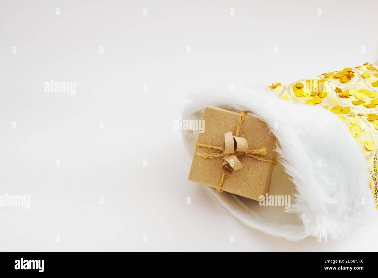 Gift box wrapped in kraft paper and tied sack rope in yellow christmas sock on white background Stock Photo
