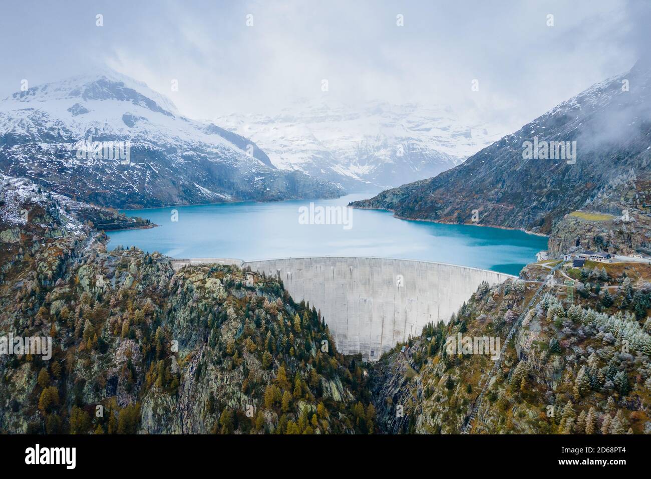 Hydropower generated from arch dam and reservoir lake in snow covered Swiss Alps mountains to produce renewable energy, sustainable hydroelectricity, Stock Photo