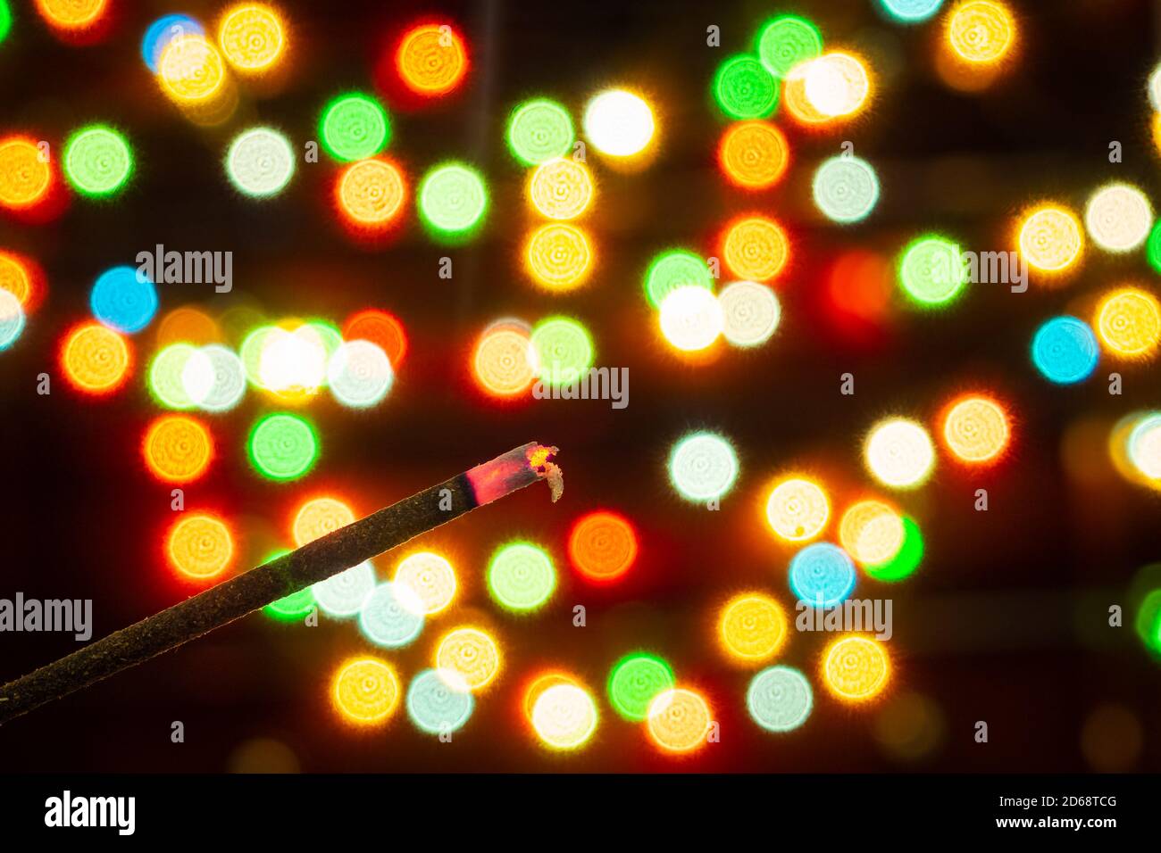 Incense stick on the background of bokeh of colorful lights of garlands, blurred backdrop, selective focus Stock Photo