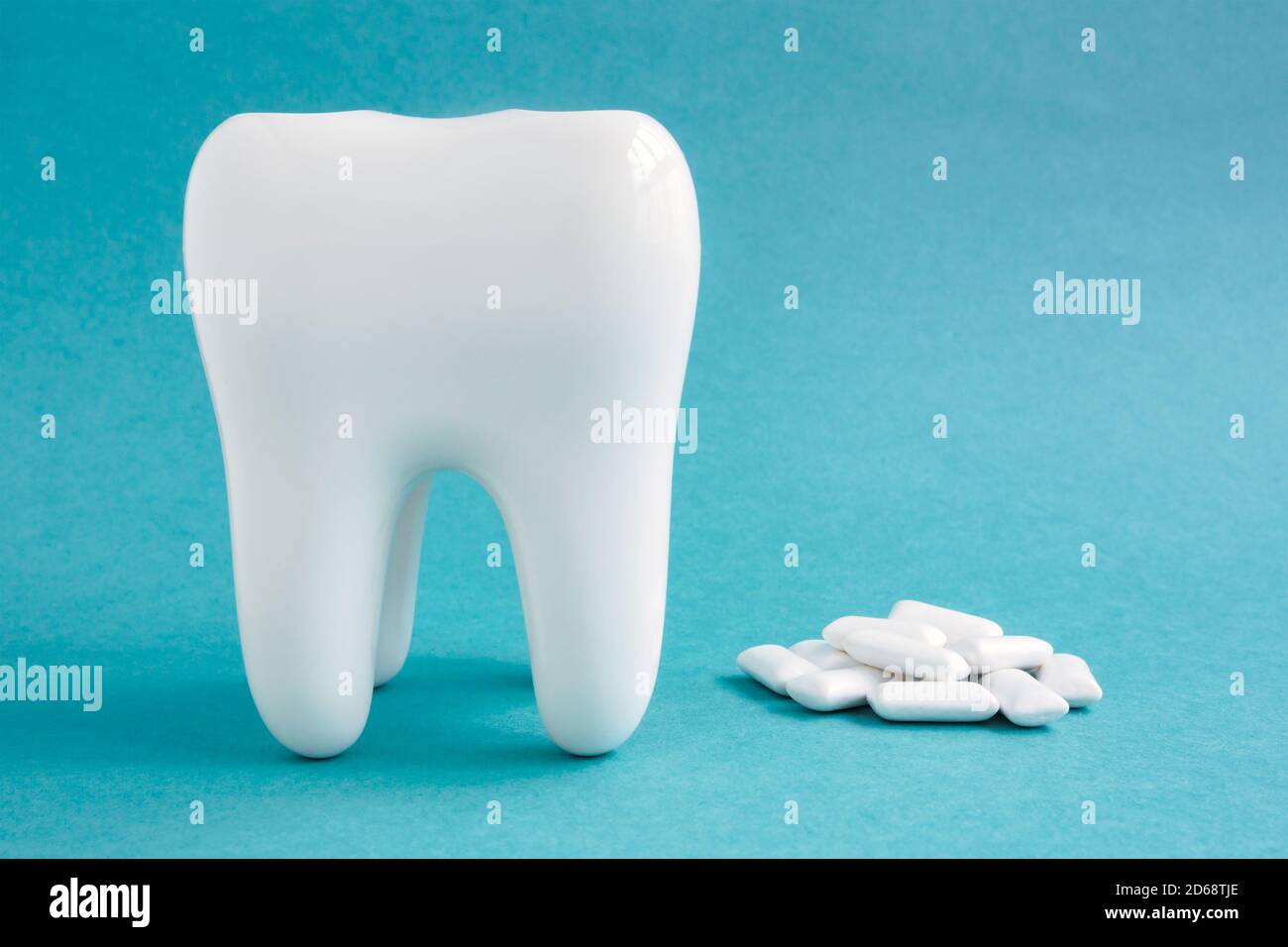 White healthy tooth model and heap of chewing gums on blue background