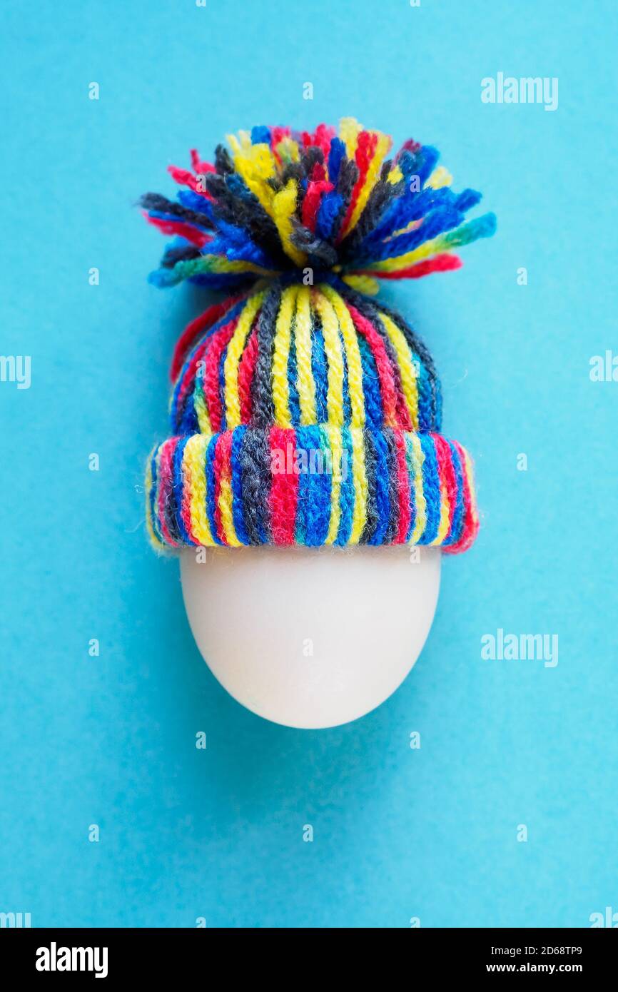 white egg in knitted wool colored hat on blue background, easter concept, vertical top view Stock Photo