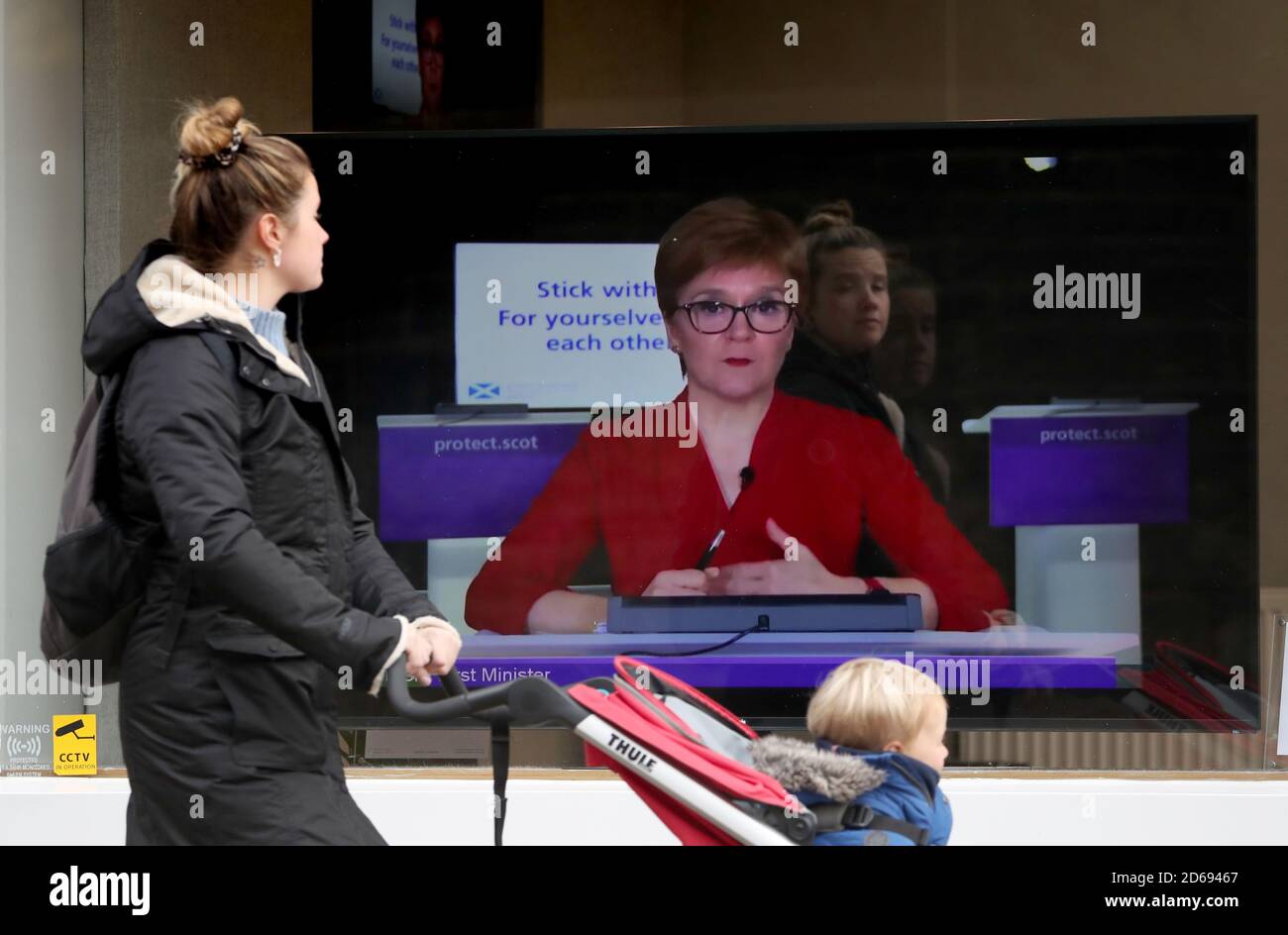 A member of the public walks past a tv screen at The Sound Counsel in  Edinburgh as First Minister Nicola Sturgeon takes part in a virtual sitting  of the Scottish Parliament after