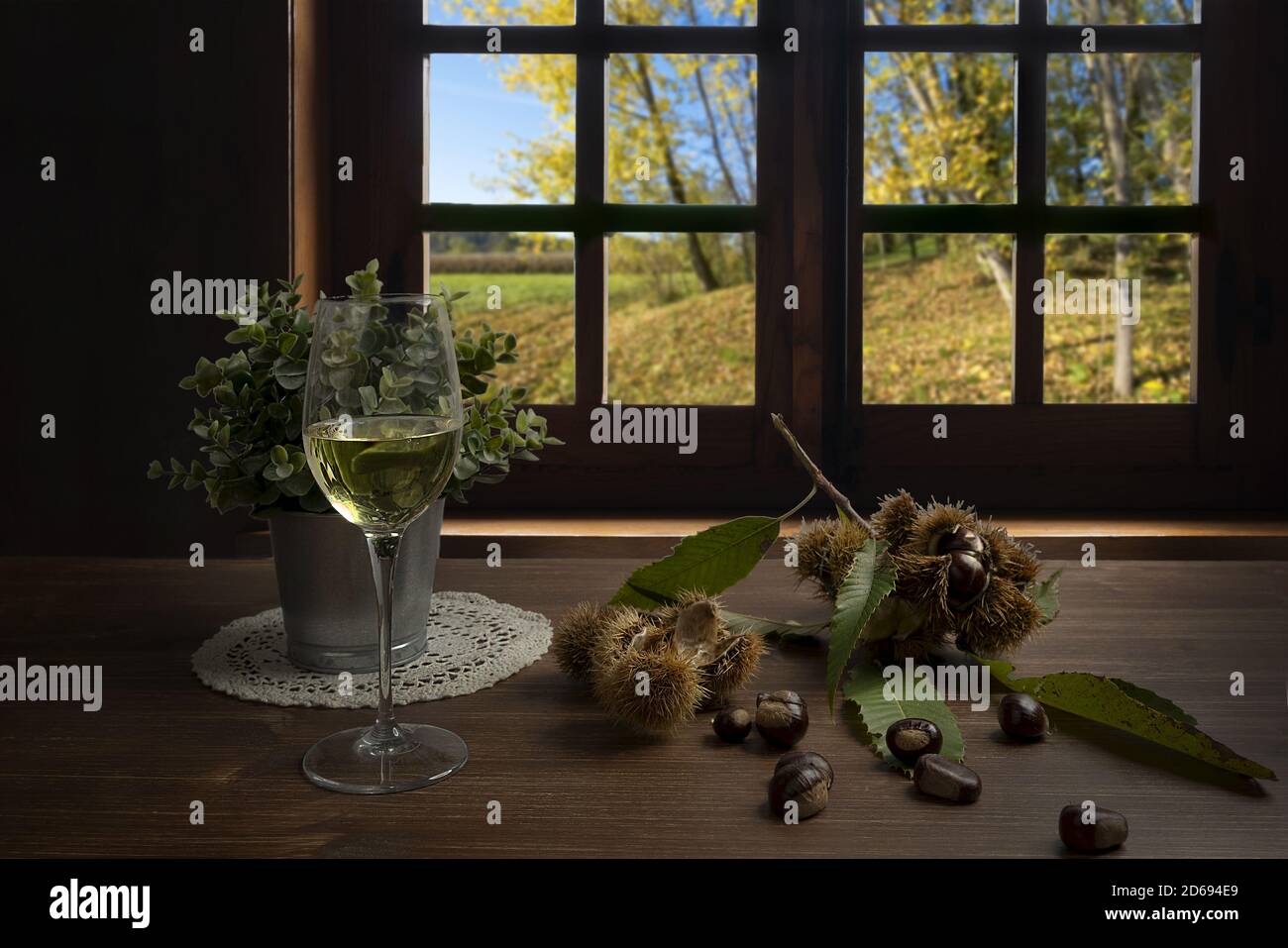 chestnuts and a glass of white wine on the table in front of the window on an autumn day Stock Photo