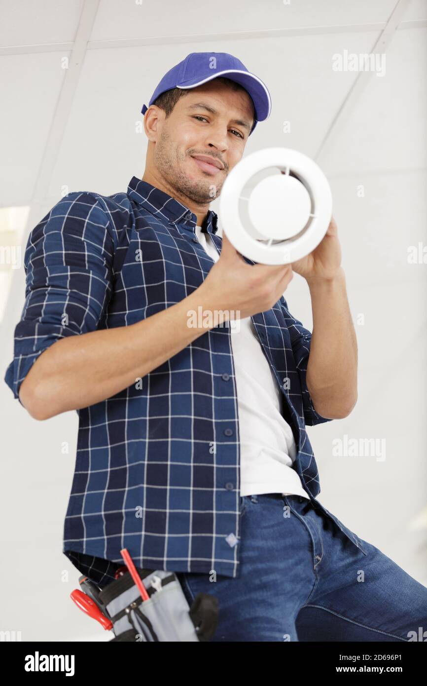 handsome young man electrician cleaning air filter on a ladder Stock Photo