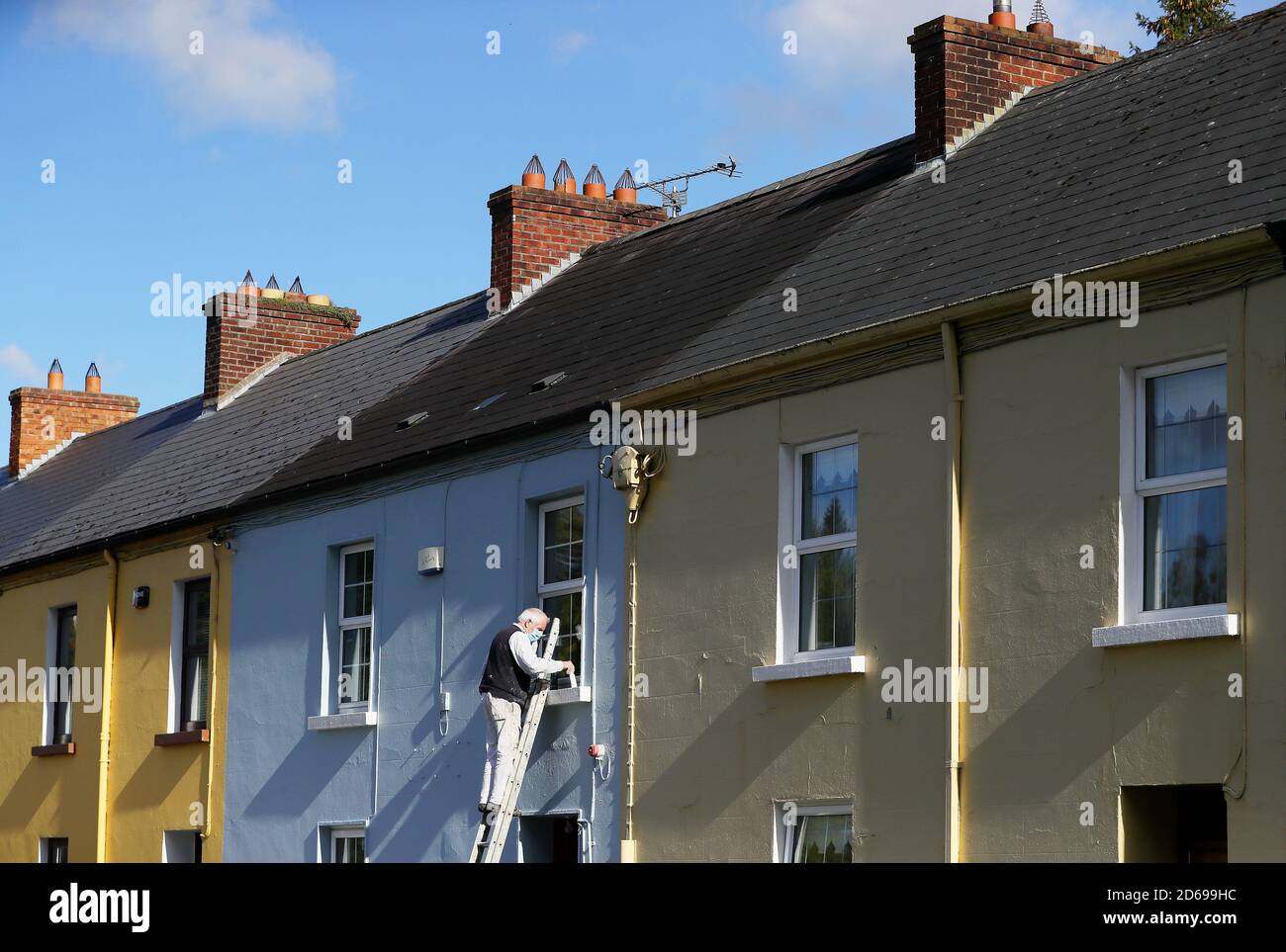 A man wearing a face mask paints the front of a house on Main street, Co. Cavan, as counties Donegal, Cavan and Monaghan prepare to move to Level 4 of Ireland's Covid-19 plan from midnight tonight. Stock Photo