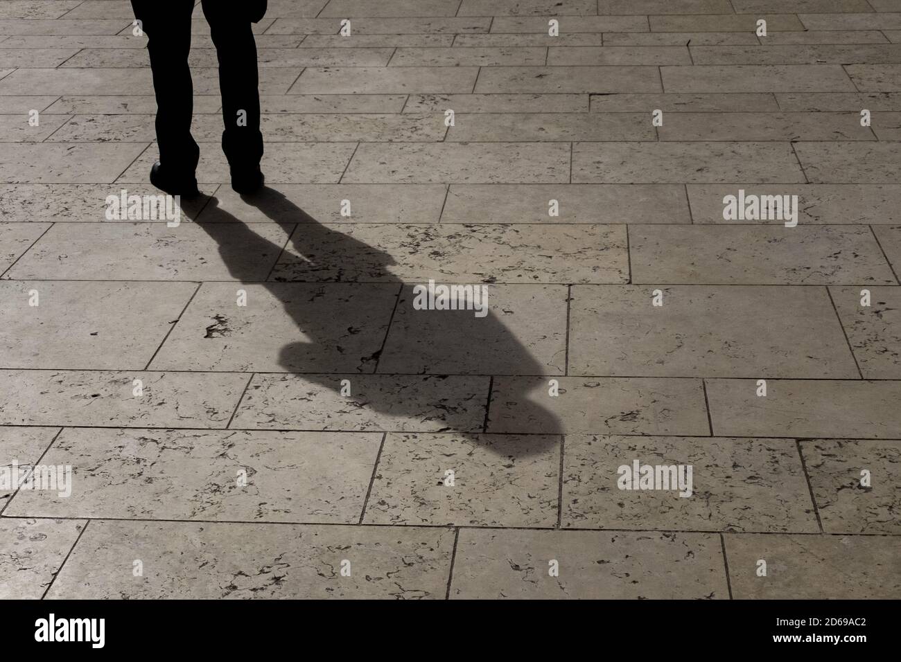 A pedestrian stands casting a long shadow in the spring afternoon sunshine against the stone slabs in the town’s square in the centre of Bournemouth in Dorset. 04 April 2014. Photo: Neil Turner Stock Photo