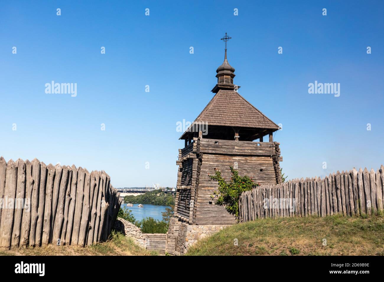 Watchtower in wooden medieval Zaporozhian Sich historical complex, view on DneproGES power station with blue clear bright sky. Khortytsia island on Dn Stock Photo