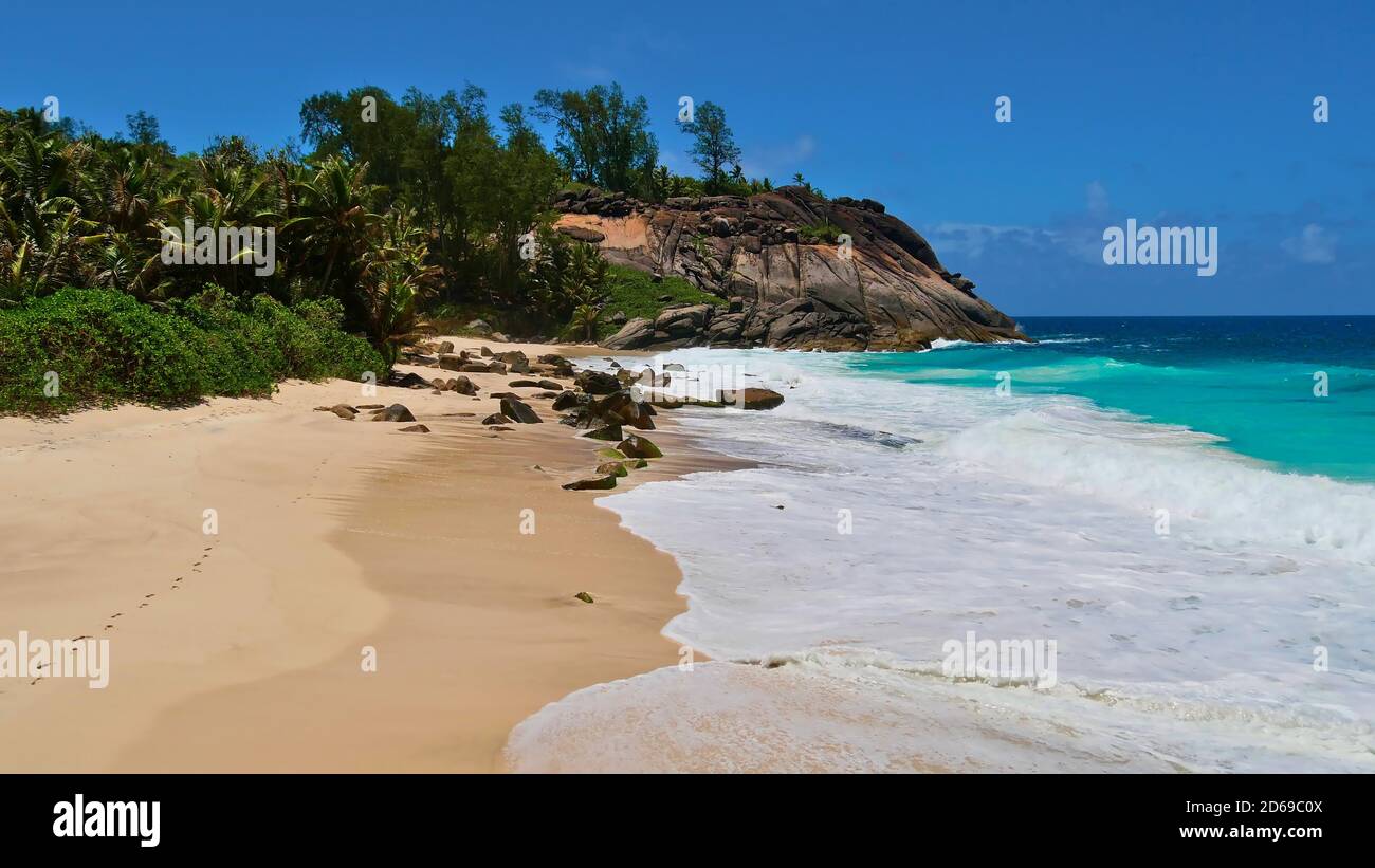 Tropical beach Anse Capucins in the south of Mahe island, Seychelles with footprints in the sand, turquoise colored water and granite rock formations. Stock Photo