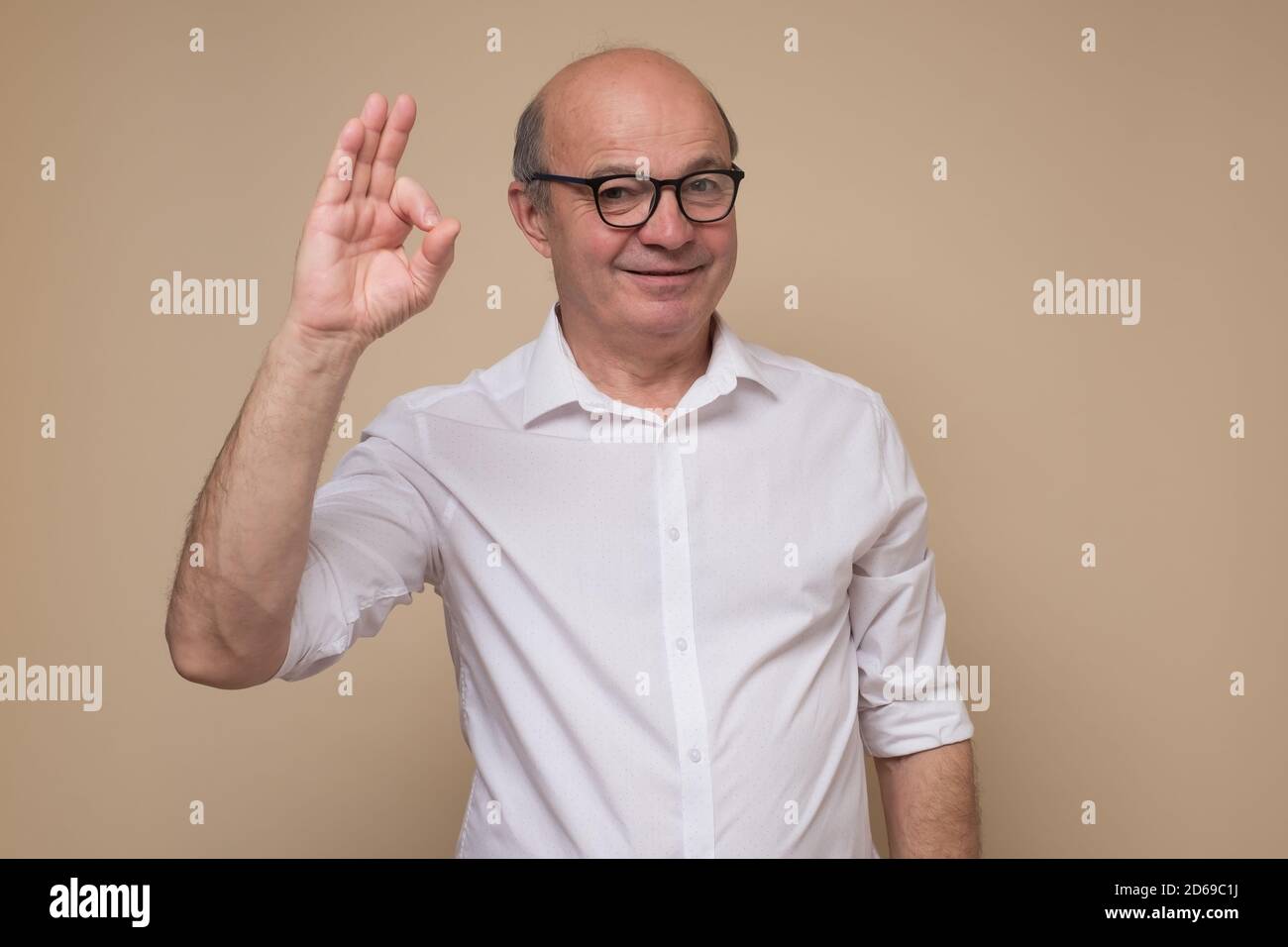 Happy mature bald man in glasses doing ok gesture. Stock Photo