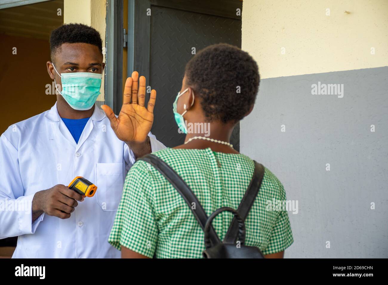 african school teacher stops a pupil for body temperature check before entering the classroom Stock Photo