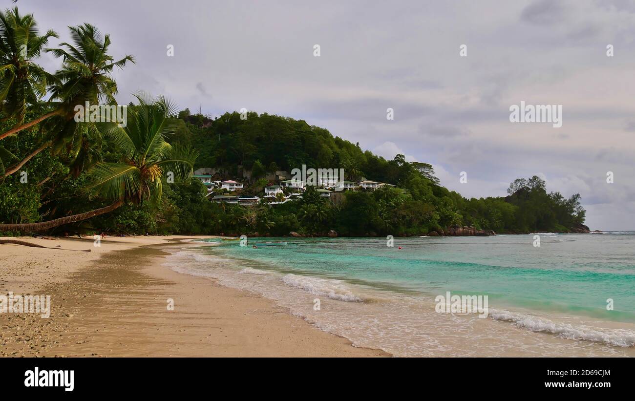 Tourists enjoying their holidays on tropical beach in Baie Lazare, Mahe island, Seychelles with turquoise colored water, coconut trees, docking boats. Stock Photo