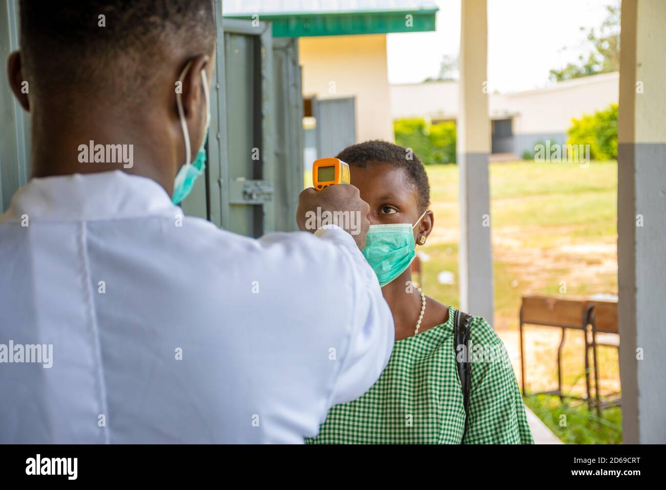 a teacher in an african school checking pupil's body temperature before she enters the classroom Stock Photo