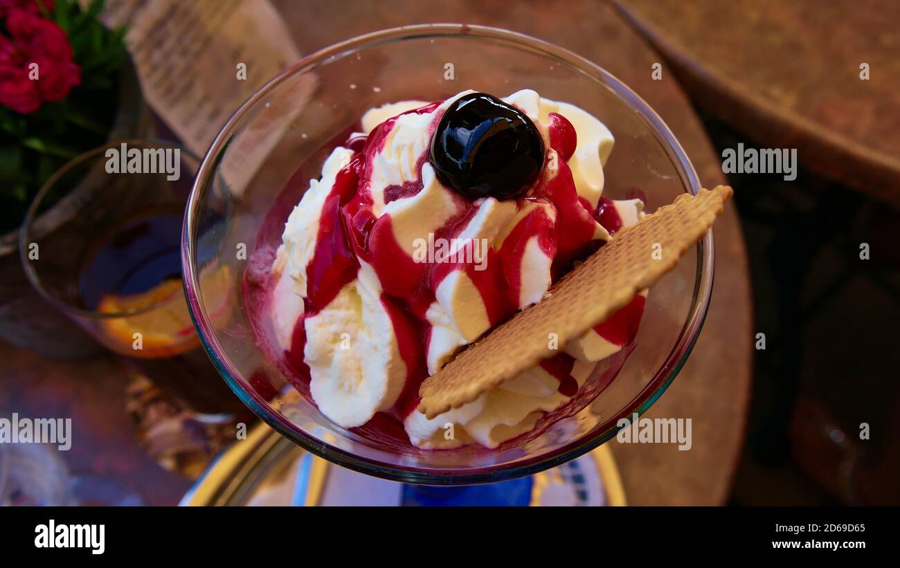 https://c8.alamy.com/comp/2D69D65/close-up-view-of-delicious-ice-cream-sundae-cup-with-red-sauce-whipped-cream-waffle-and-cherry-on-top-standing-on-a-cafe-table-with-glass-of-soda-2D69D65.jpg
