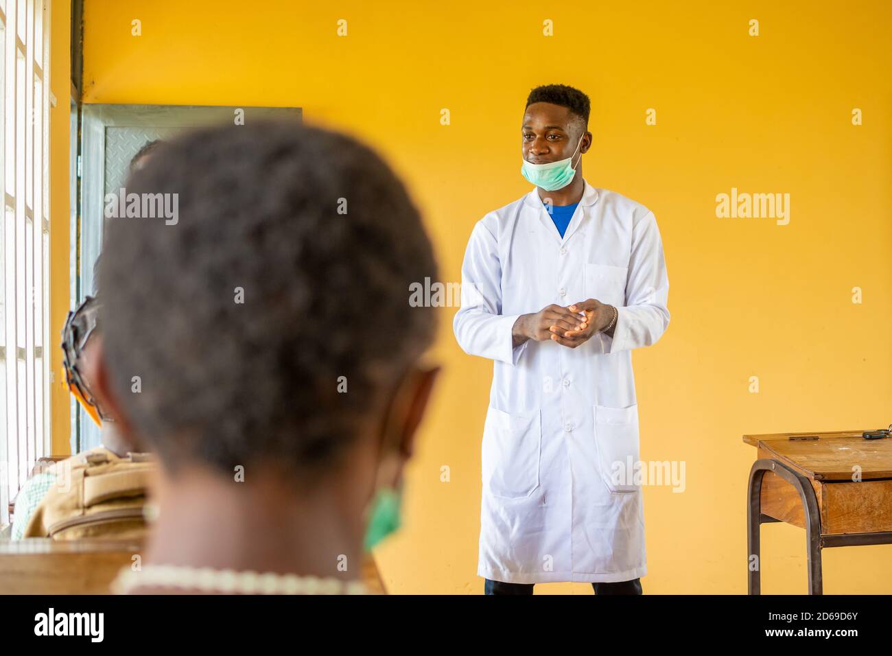 african high school teacher wearing a lab coat and face mask in class ...