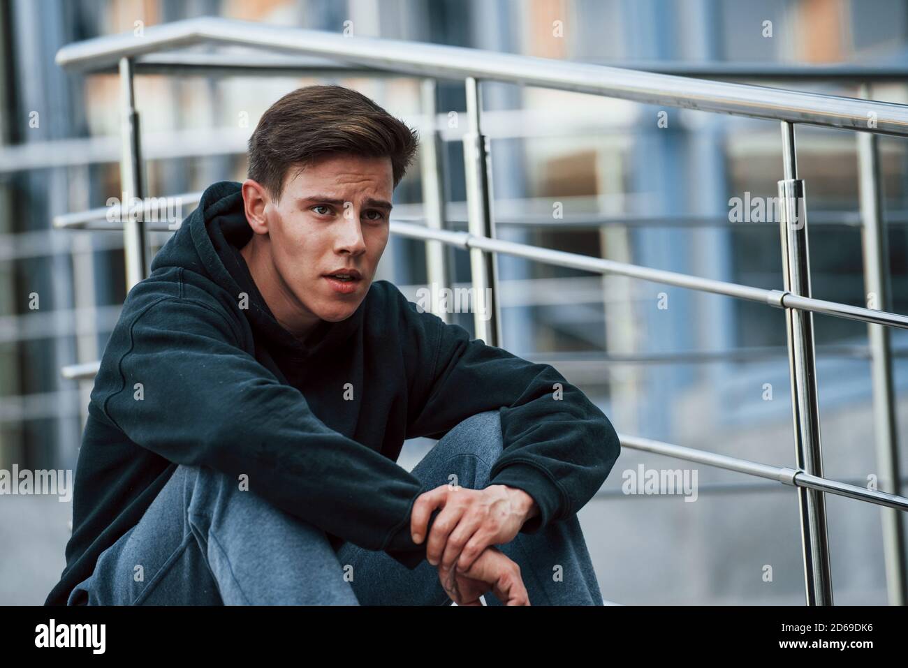 Portrait of young main in black clothes that sits on the stairs and taking a break Stock Photo