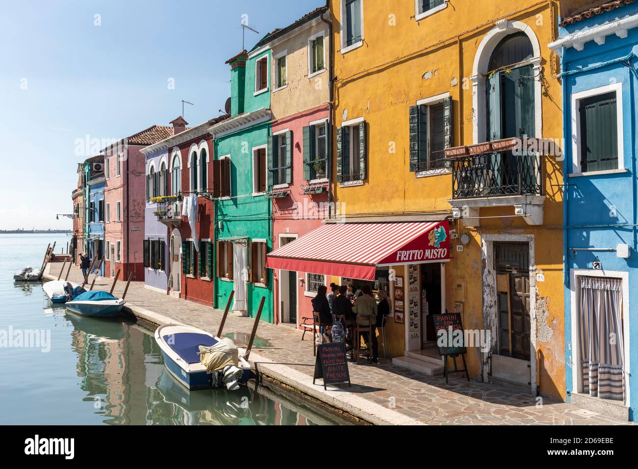 The Venetian Lagoon island of Burano and its colourful picturesque buildings and restaurant with boats moored in the canal.  Venice, Italy. 2020 Stock Photo