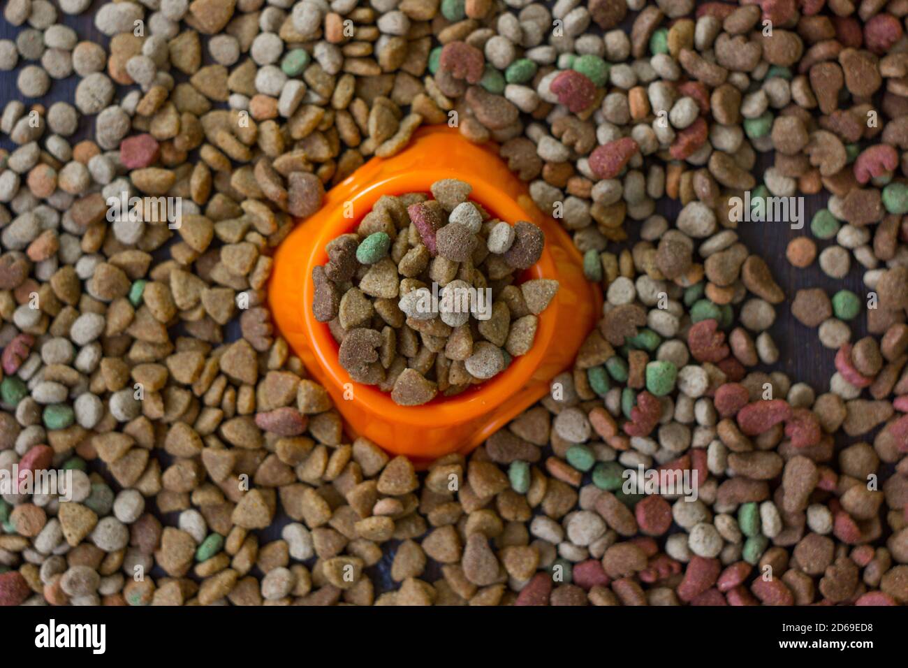 Orange plastic bowl filled with dry pet food surrounded by dry food for