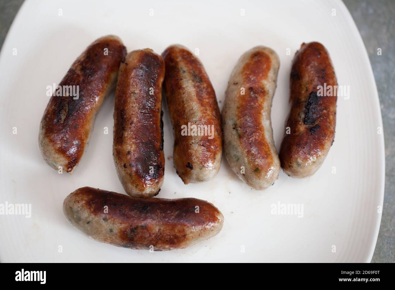 Half a dozen cooked British pork sausages on a white plate Stock Photo