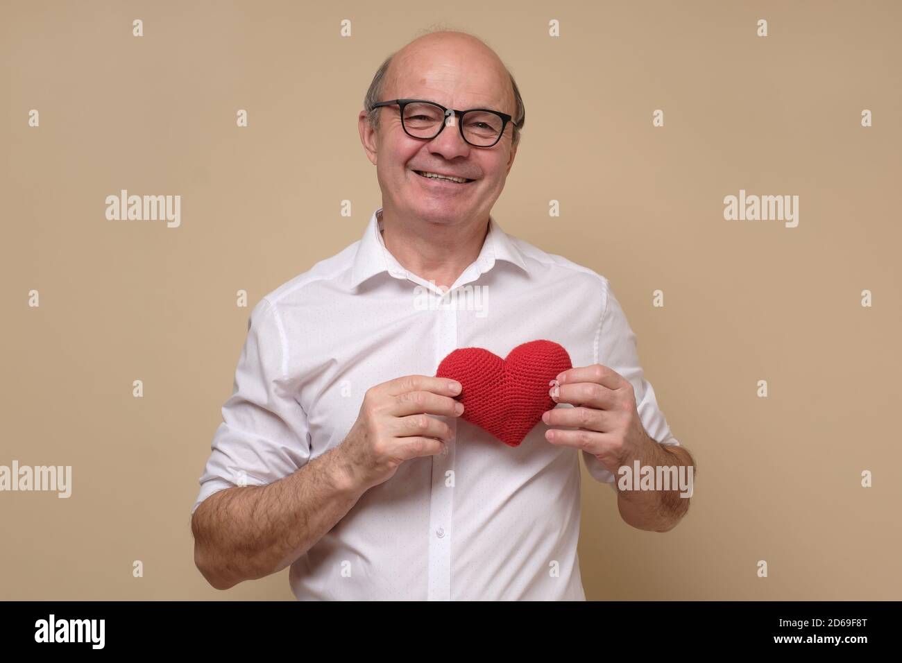 Senior gentleman in glasses holding a red heart smiling. Stock Photo