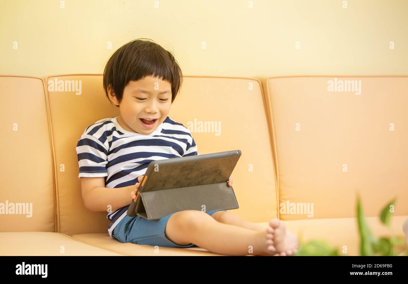 Happy boy sitting on couch with Tablet computer Stock Photo