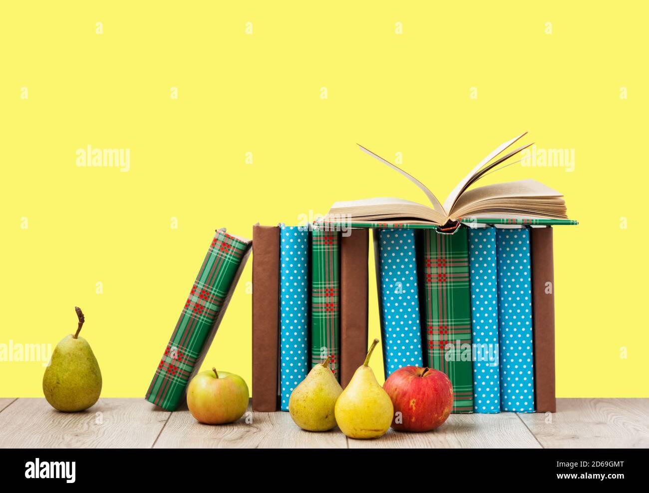 Open book textbook in colorful cover, pears and apples on a yellow ...