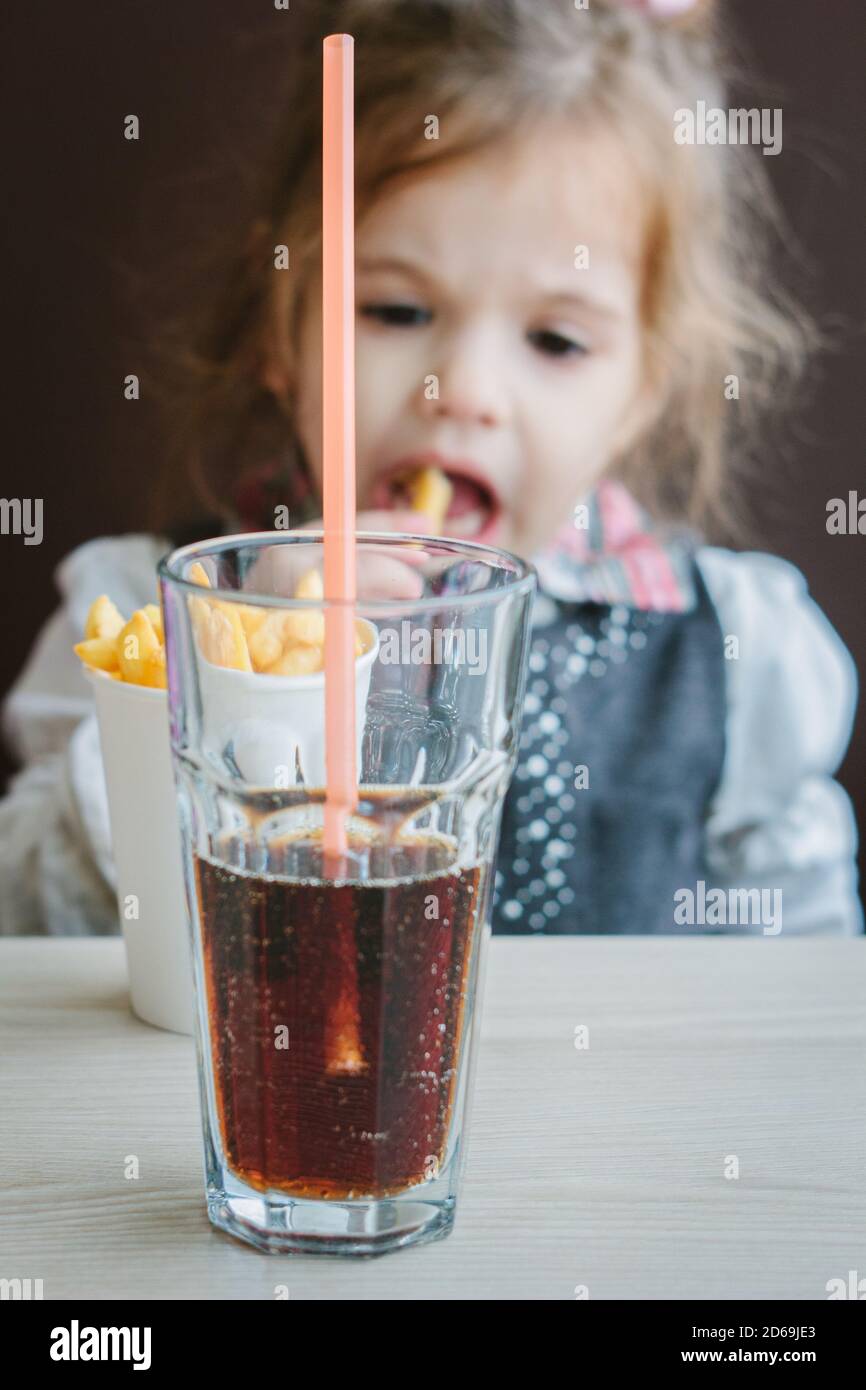 Little girl in a restaurant eating french fries and drinking cola Stock Photo