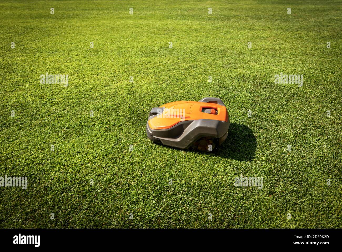 Automatic orange and grey lawn mower robot moves on the green grass, side view, photography. Stock Photo