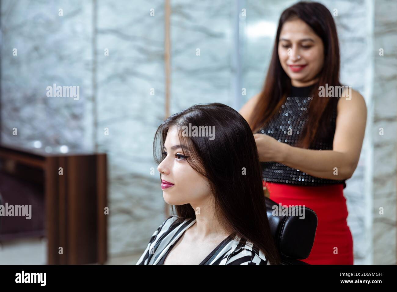 A hair dresser provides hair styling services to a pretty young Indian woman, beautiful woman gets her hair done at a salon, selective focus. Stock Photo