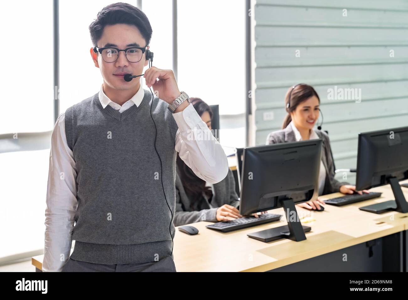 Portrait of Young adult friendly and confidence operator man with headsets and his team working in a call center as customer service and technical Stock Photo