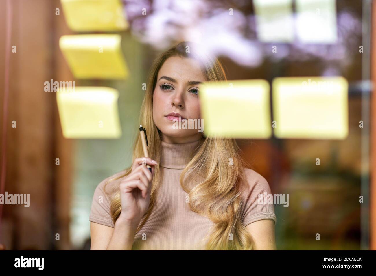 Young businesswoman brainstorming with notes on a glass wall in an office Stock Photo