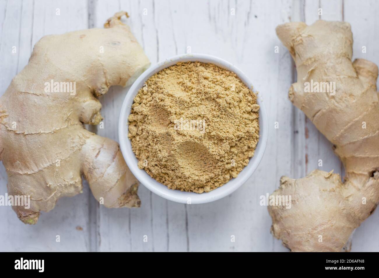 Grounded ginger and ginger root on white wooden surface. Stock Photo