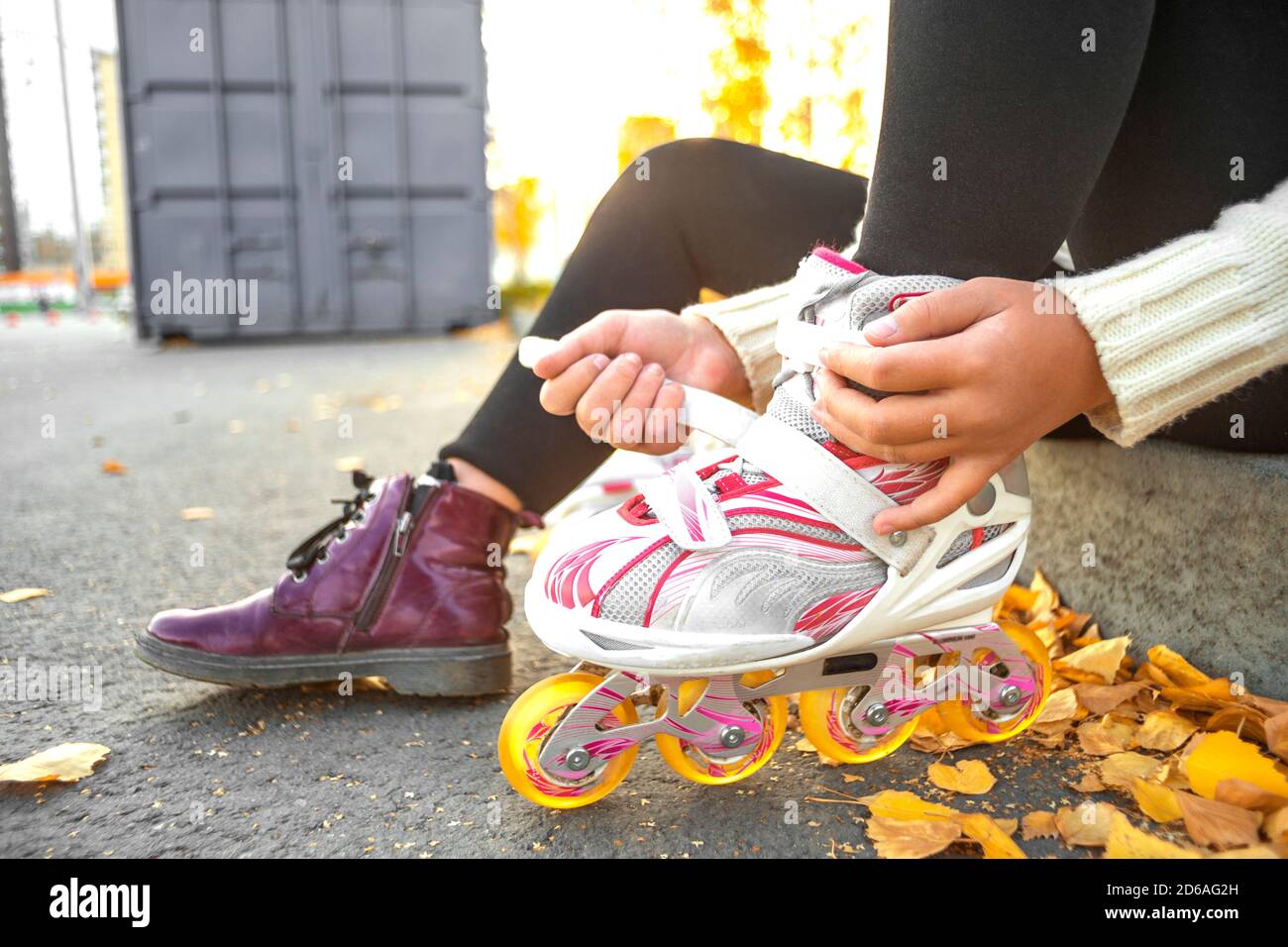 A girl puts on roller skates sitting on a concrete curb. Child fastens