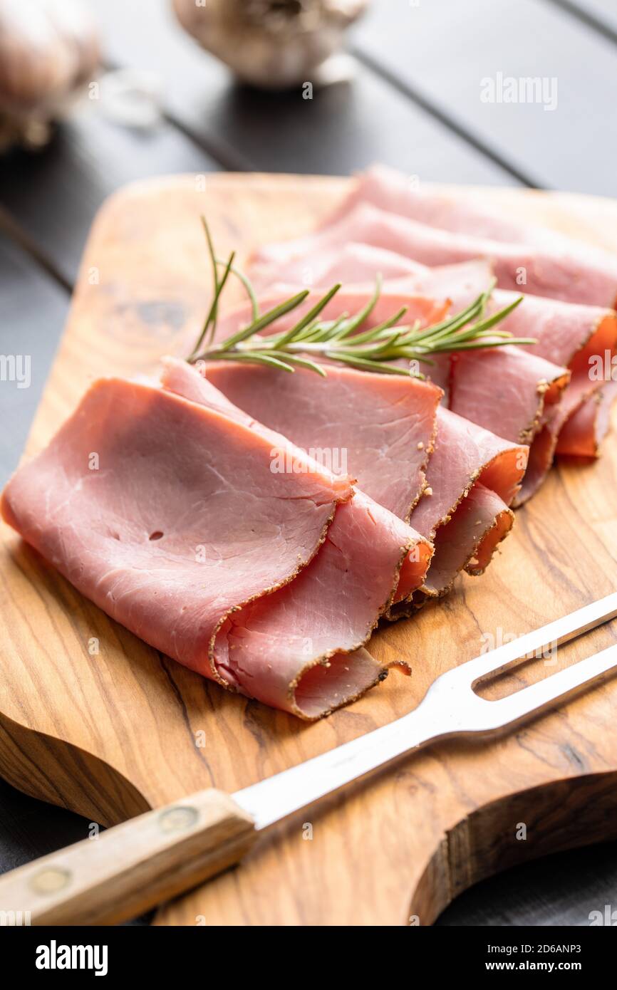 Sliced beef ham on cutting board on black table. Stock Photo