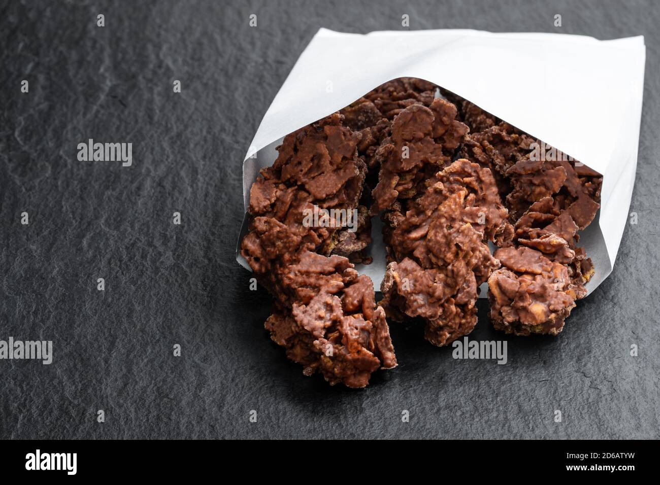 Chocolate  corn flake clusters in paper bag on black stone background Stock Photo